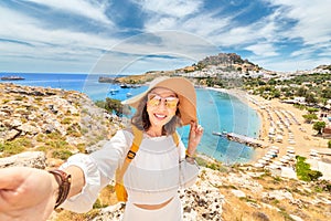 Happy woman tourist taking selfie photo on her smartphone with view on a sandy beach and old town. Vacaction and travel