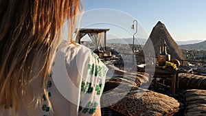 Happy woman tourist walking on terrace. Authentic beakfast setting on sunrise with amazing view of Cappadocia