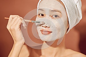 Happy woman with a towel on her head apply a cleansing mask on her face