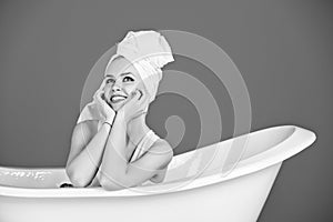 Happy woman with towel turban sitting in white bathtub