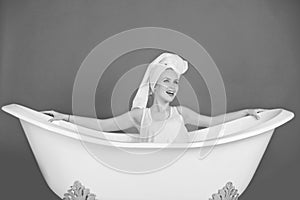 Happy woman with towel turban sitting in white bathtub