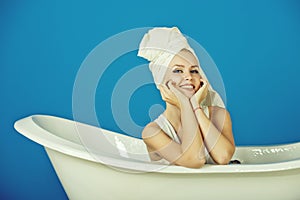 Happy woman with towel turban sitting in white bathtub