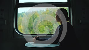 Happy woman in the train. Female traveler staring at mountains through train window and enjoying fog over mountain peaks