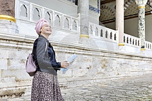 Happy woman traveler holding in her hands map and  looks beautiful view of Topkapi Palace, Istanbul, Turkey.