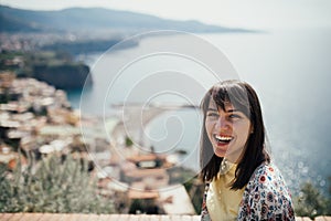 Happy woman traveler smiling at italian coast view.Woman traveling to European south coast.Enoying sunny weather medditerranean photo