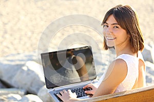 Happy woman typing on a laptop and looking at camera