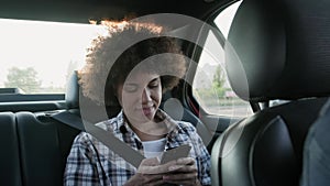 Happy woman typing message on the phone in the backseat of a car. Slow motion