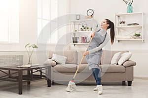 Woman in uniform cleaning home with mop and having fun