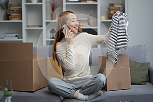 Happy Young Woman Unpacking Clothes While on Phone at Home photo