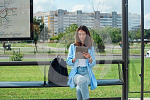 Happy woman uses a tablet or ebook on a tram station while waiting for public transport.