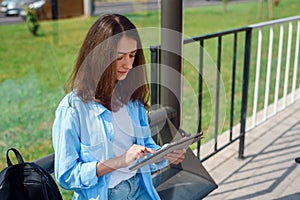 Happy woman uses a tablet or ebook on a tram station while waiting for public transport.