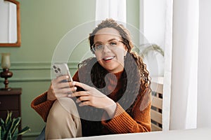 Happy woman using cell phone technology at home, smiling while checking apps on her smartphone and relaxing with cellular devices