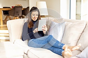 Happy woman using digital tablet while relaxing at home on the sofa