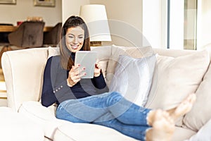 Happy woman using digital tablet while relaxing at home on the sofa