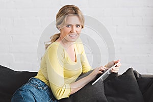 happy woman using digital tablet and smiling at camera while sitting