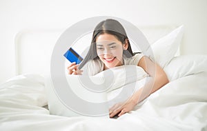 Happy woman using her credit card on the web lying doing shoppin