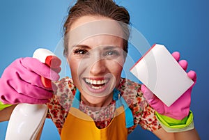 Happy woman using kitchen sponge and cleaning detergent on blue