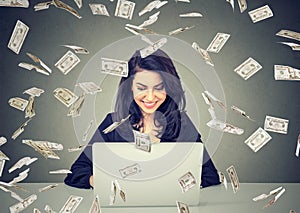 Happy woman using a laptop building online business under dollar bills falling down.