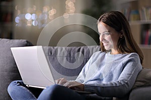 Happy woman using laptop on a couch at home in the night