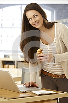 Happy woman using laptop eating croissant