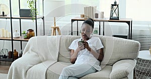 Happy woman using mobile phone relaxing on sofa