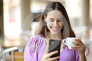 Happy woman using phone drinking coffee in a terrace