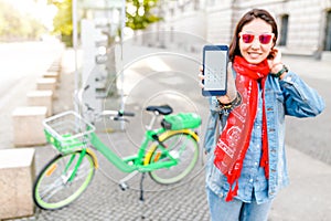 Happy woman using smart phone and rent mobile application to share modern green electric bicycle, alternative eco