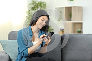 Happy woman using a smart phone sitting on a sofa