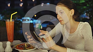 Happy woman using smartphone and messaging sitting in restaurant at night
