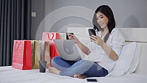 Happy woman using smartphone for online shopping with credit card on bed