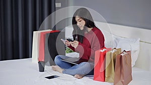Happy woman using smartphone for online shopping with credit card on bed