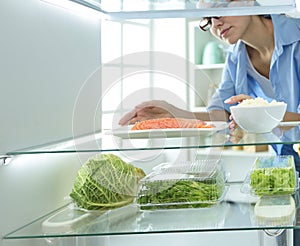 Happy Woman With Vegetables In Front Of Open Refrigerator