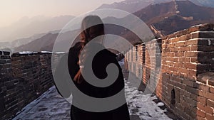 Happy woman walk at Great Wall of China, come down from watch tower at Badaling section at sunset in winter. Travel