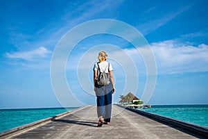 Happy woman walking along the wooden pier with blue sea and sky background