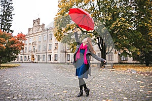 Happy woman walking in autumn city park. Rainy weather and yellow trees around