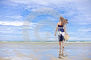 Happy Woman walking on the beach in summer vacation wearing hat and dress enjoying the view at the island beach