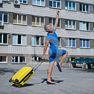 Happy woman walking down the street holding yellow suitcase with wheels