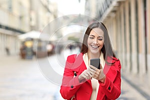 Happy woman walking using smart phone in the street