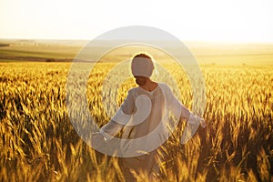 Happy woman walks over wheat field in the rays