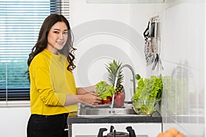 Happy woman washing vegetables in the sink in the kitchen at home