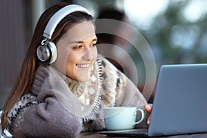 Happy woman watching and listening media on laptop in a bar