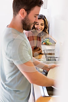 Happy woman watching man washing dishes