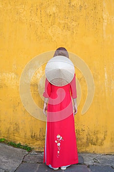 Happy woman wearing Ao Dai Vietnamese dress and hat, traveler sightseeing at Hoi An ancient town in central Vietnam. landmark and