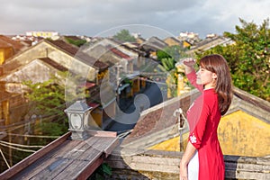 Happy woman wearing Ao Dai Vietnamese dress, traveler sightseeing view at rooftop in Hoi An ancient town. landmark and popular for