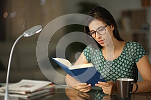Happy woman wearing eyeglass reading a paper book in the night photo