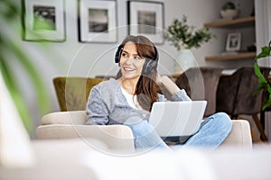 Happy woman wearing headphone and using laptop while relaxing at home