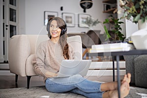 Happy woman wearing headphone and using laptop while relaxing at home
