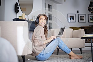Happy woman wearing headphone and using laptop while relaxing at home