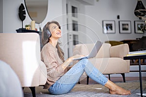 Happy woman wearing headphone and using laptop while relaxing at home