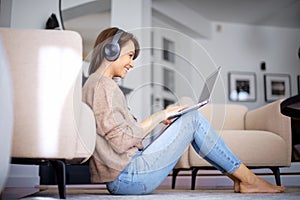 Happy woman wearing headphone and using laptop while relaxing at home